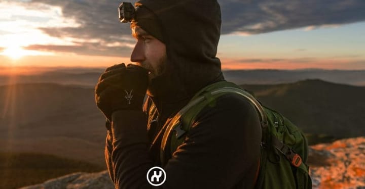Outdoor adventurer using Nuyarn merino wool hoodie for warmth during a cold sunrise hike