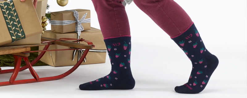 Person wearing navy socks with berry pattern while setting gifts on a sled, representing lifetime-warranty hiking socks.