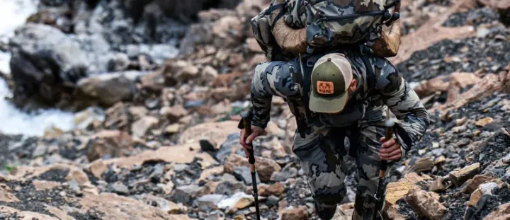 Hunter wearing KUIU performance jacket and pack in mountain terrain during the 2025 Black Friday Sale, promoting up to 50% off ultralight hunting and backcountry gear.