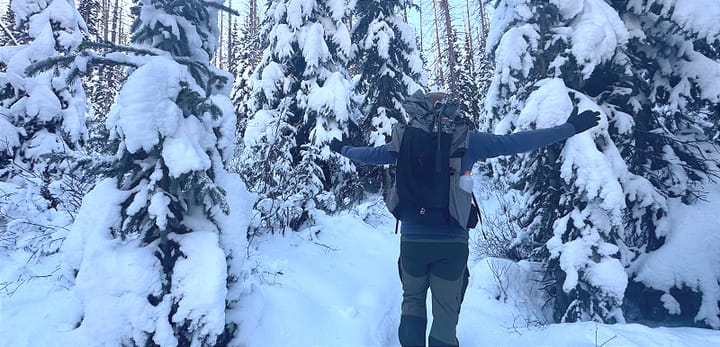 Backpacker wearing the Outdoor Vitals Shadowlight Carbon 60 in a snow-covered forest with arms outstretched, showing pack fit and winter performance.