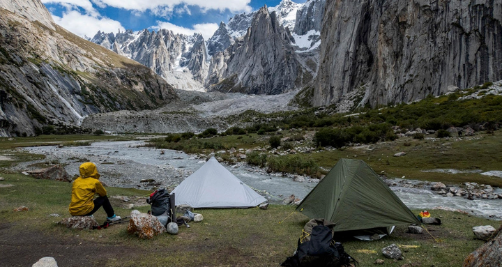 Backpacker setting up a Six Moon Designs Lunar tent in a mountain campsite during the 2025 Holiday Sale, offering 25% off all ultralight gear with code YULEHIKE.