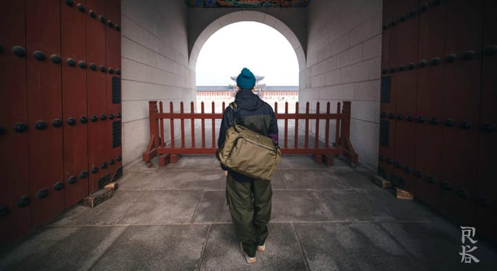 Traveler wearing a Helinox TERG everyday carry bag inside an urban architectural space, showcasing durable minimalist design built for city travel and daily use.