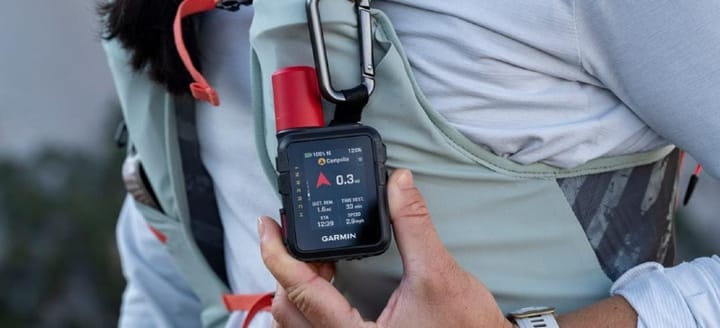 Garmin inReach Mini 3 Plus satellite communicator clipped to a backpack shoulder strap during a hike, showing compact size and hands-free backcountry safety use.