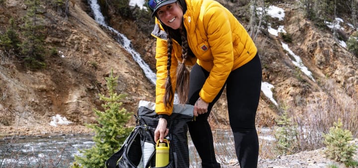 hiker wearing branwyn essential compressive leggings made of wool in black she is near a river using her backpack