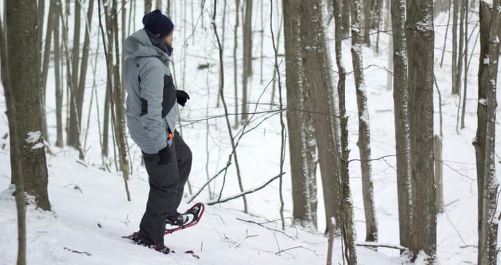 Person snowshoeing through a snowy forest wearing winter hiking gear, demonstrating traction and stability for winter trail hiking.