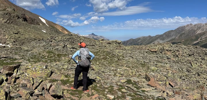 Hiker standing in wide alpine landscape with rocky tundra and distant mountain peaks under a blue sky