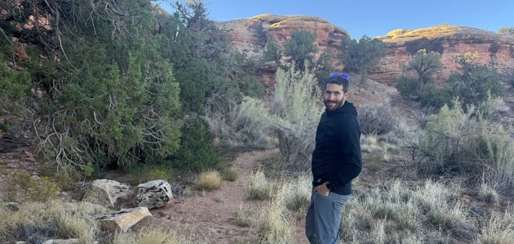 hiker wearing Outdoor Vitals Pursuit Hybrid Fleece standing on desert trail with red rock formations and scrub vegetation